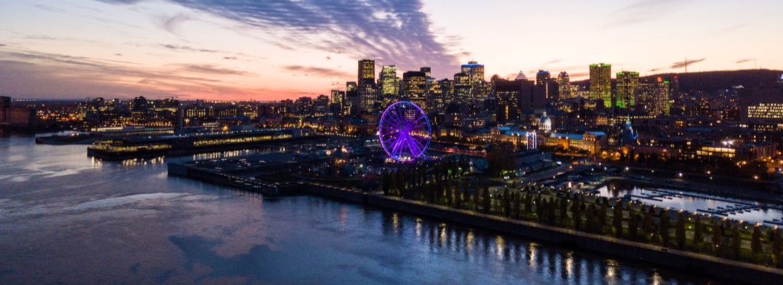 Vue aérienne du Vieux-Port de Montréal au crépuscule, avec la Grande roue illuminée et le centre-ville.